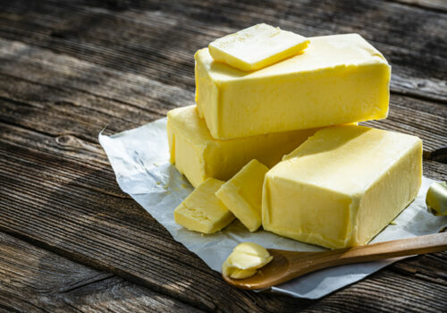 High angle view of various sticks of fresh butter with slices shot on rustic wooden table. The composition is at the right of an horizontal frame leaving useful copy space for text and/or logo at the left. High resolution 42Mp studio digital capture taken with Sony A7rII and Sony FE 90mm f2.8 macro G OSS lens